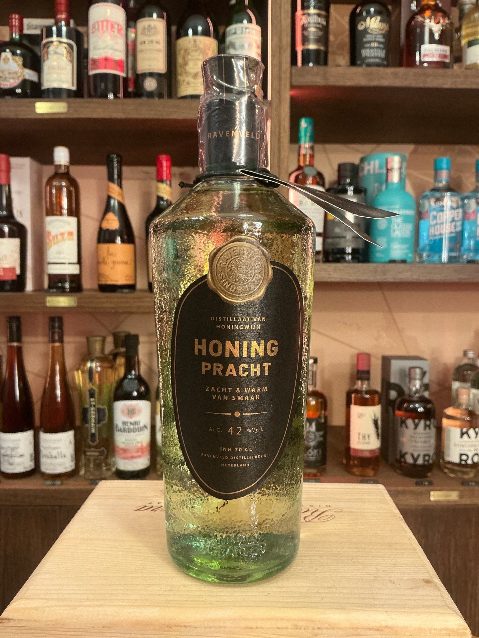 Honingpracht premium distilled gin bottle with black label and gold lettering on wooden surface with liquor shelves.