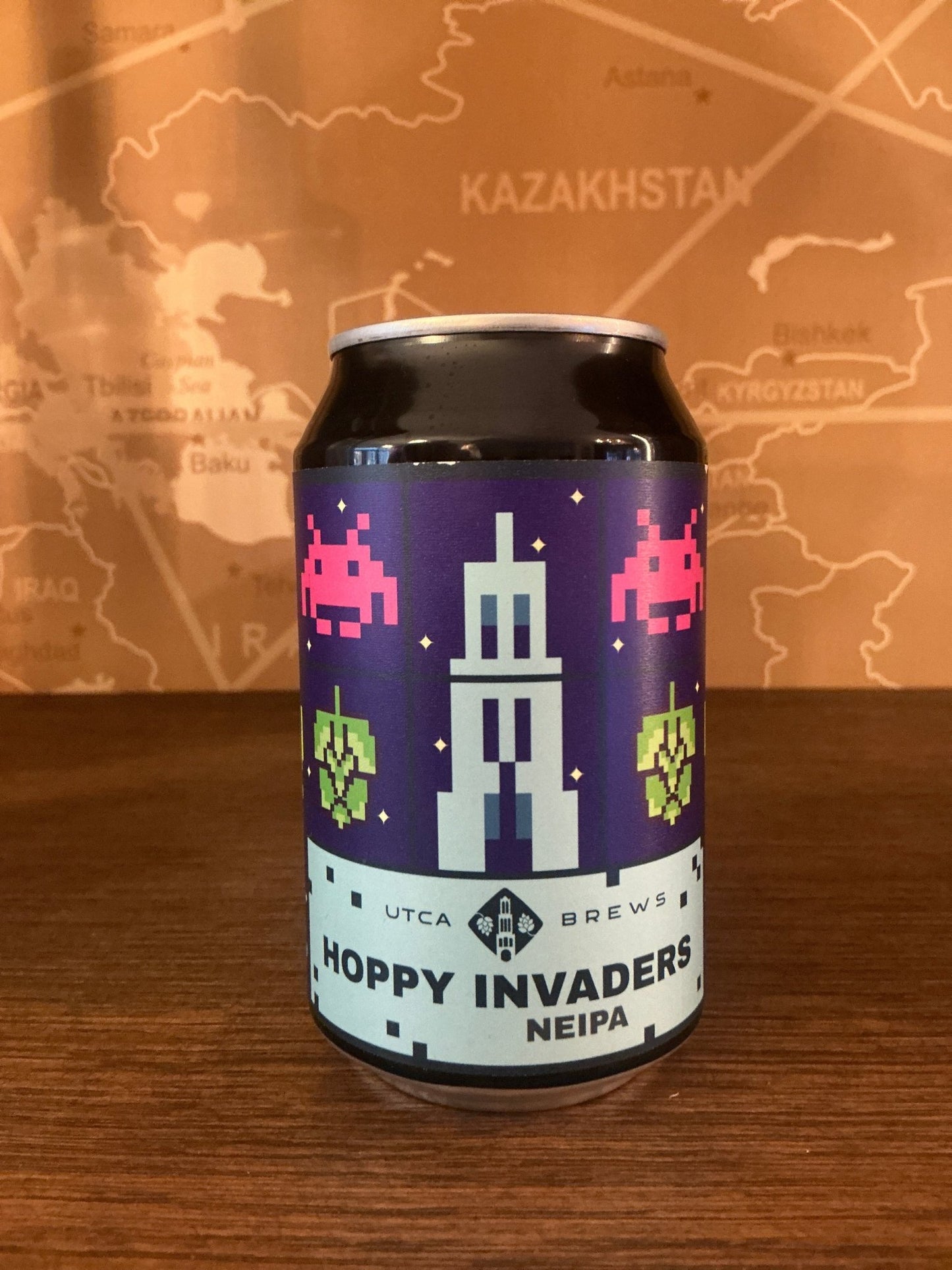 Purple and light blue can with pixel art style green and pink space invader characters, featuring a white tower illustration