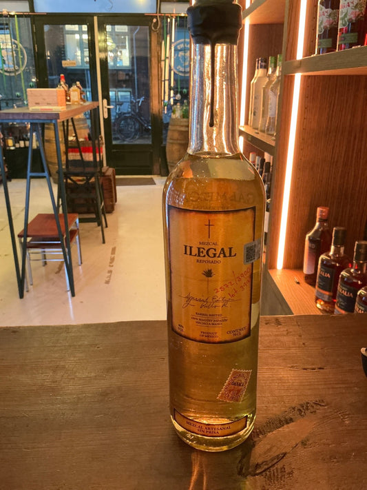 Illegal Mezcal premium small batch artisan mezcal bottle with golden amber liquid on wooden counter.