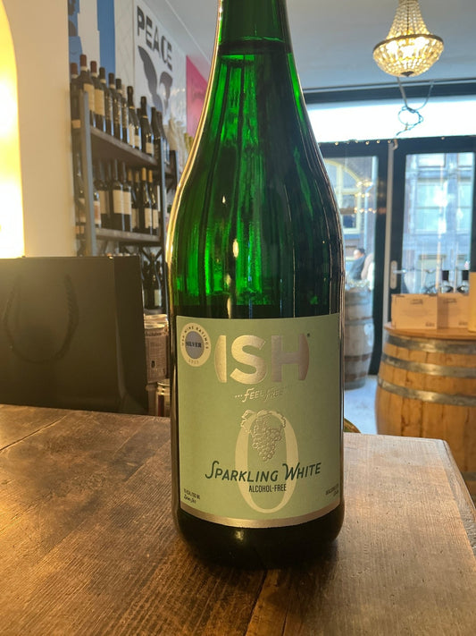 Green glass bottle of ISH Sparkling White non-alcoholic wine with light blue and white label on wooden table in artisan.