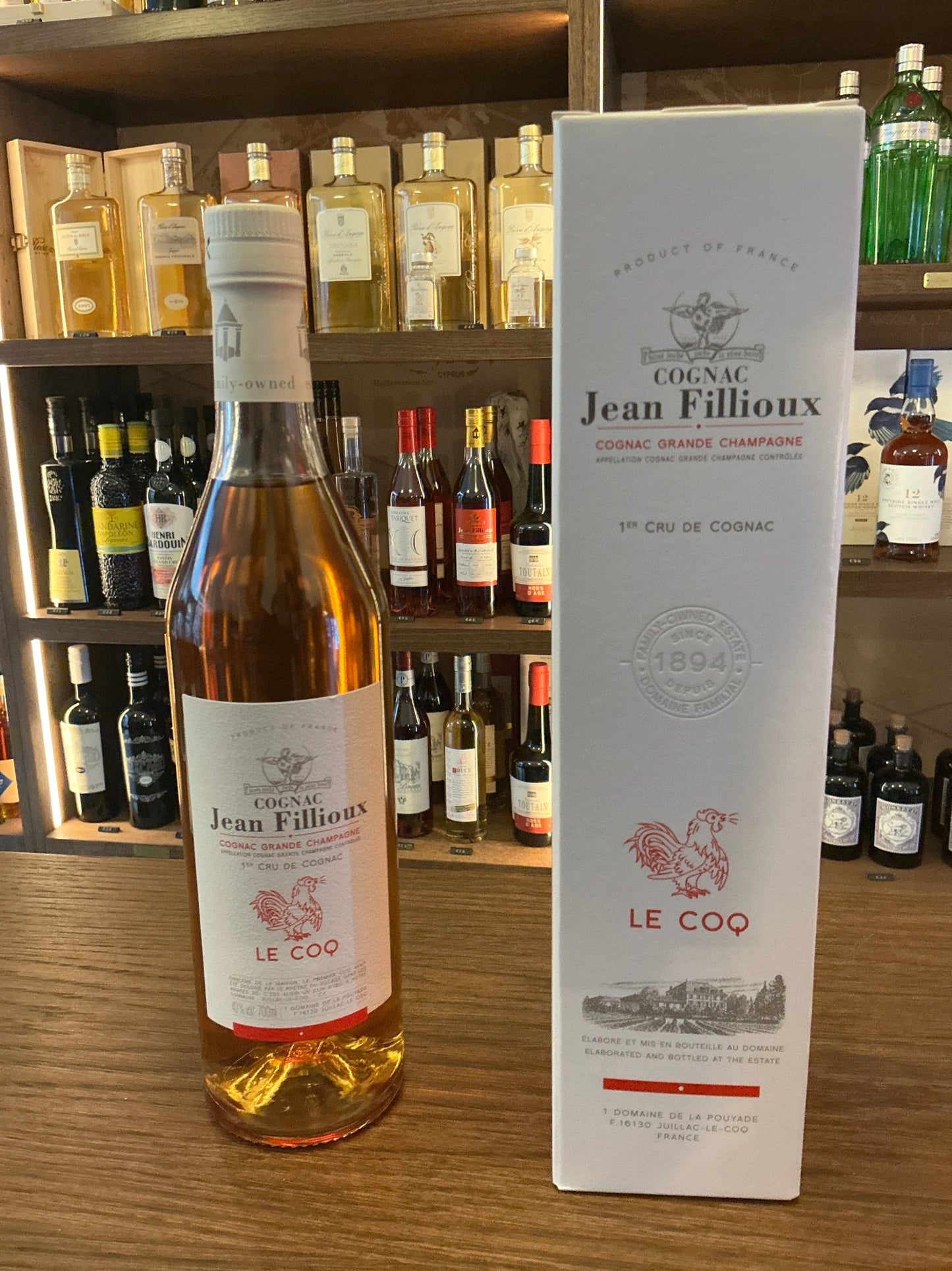Jean Fillioux Le Coq premium aged French Grand Champagne cognac bottle with white label and matching box on wooden bar shelf .