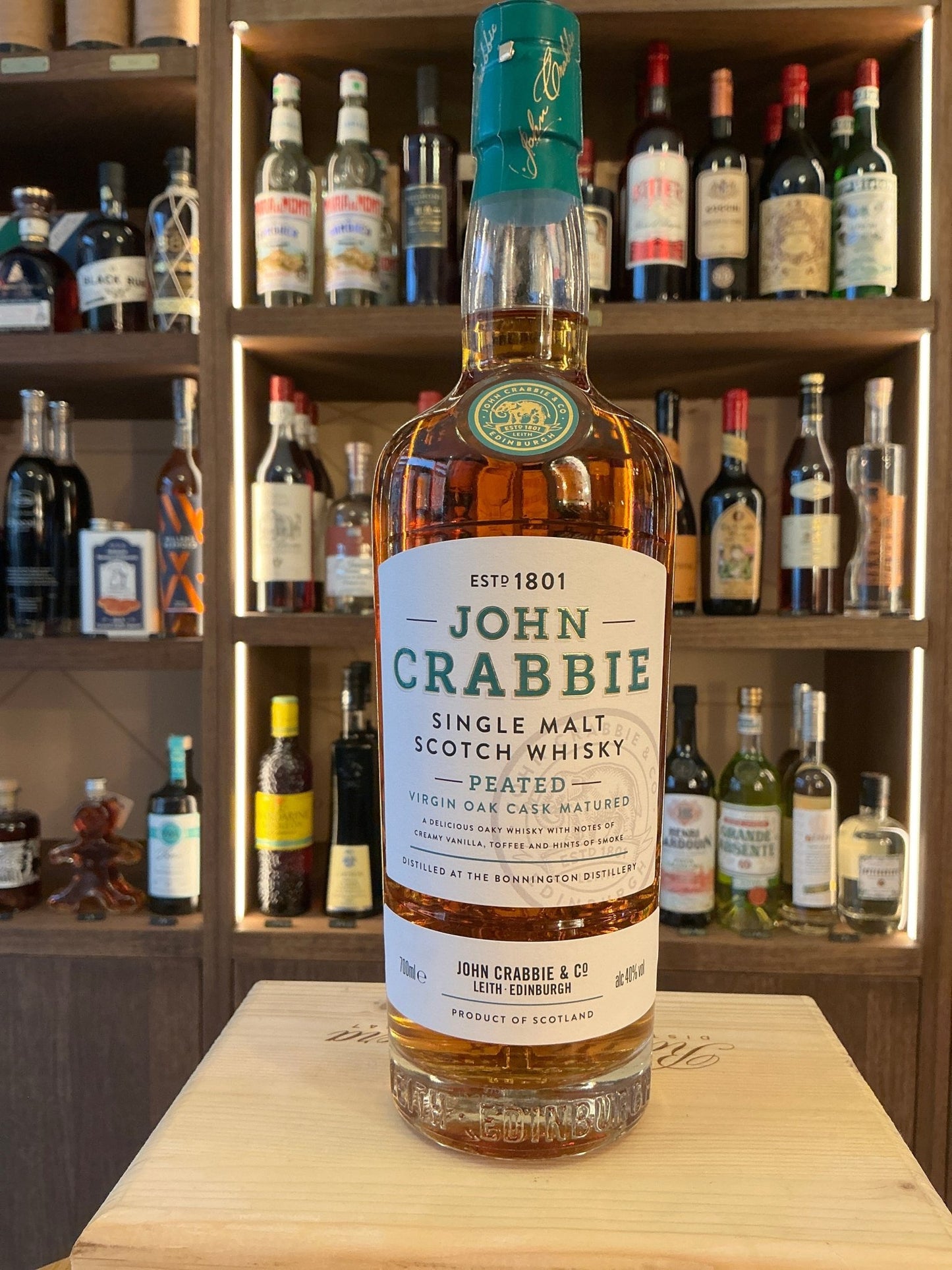 John Crabbie Single Malt Peated Virgin Oak Cask Matured Scotch whisky bottle with green cap and cream label on wooden.