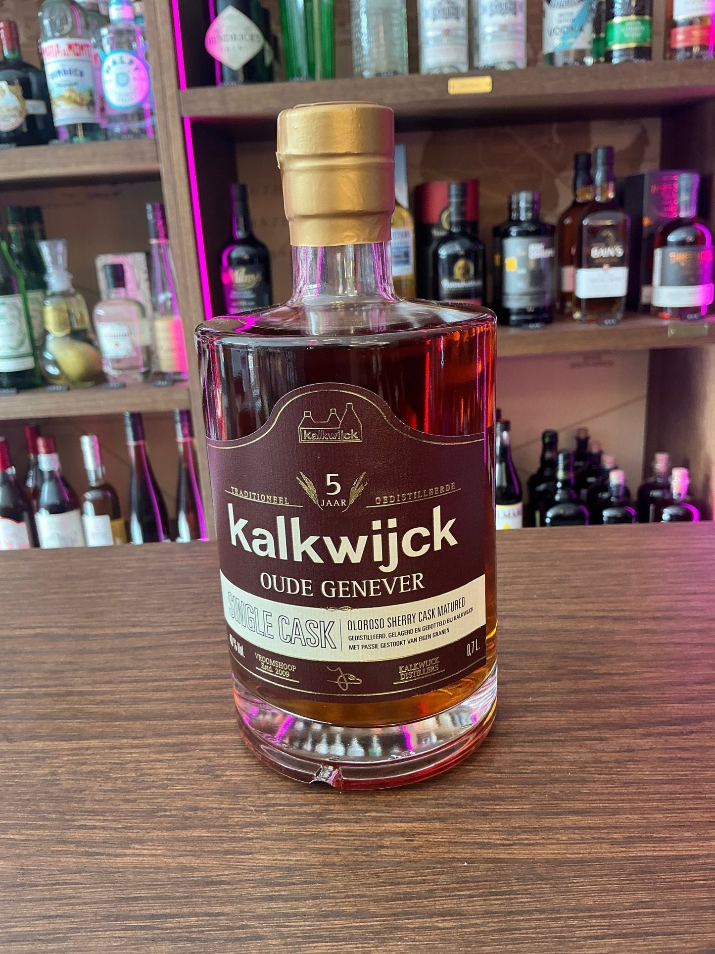 Kalkwijck 5 Yr Oude Genever bottle with dark amber aged spirit, gold cap, and artisan Dutch label on wooden surface.