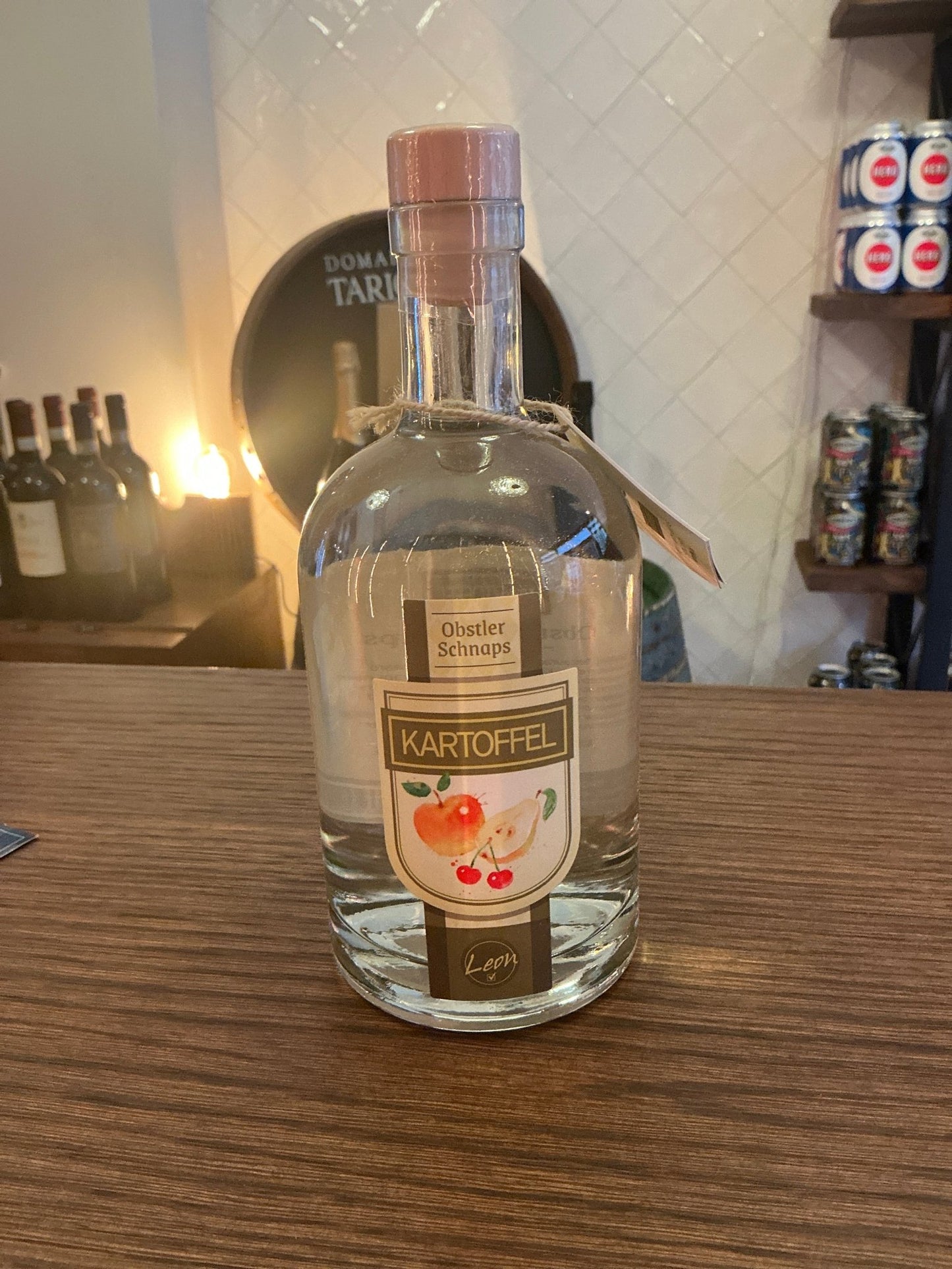 Clear glass bottle of Kartoffel Schnaps with beige label featuring red cherries, sealed with light pink cap, artisan.