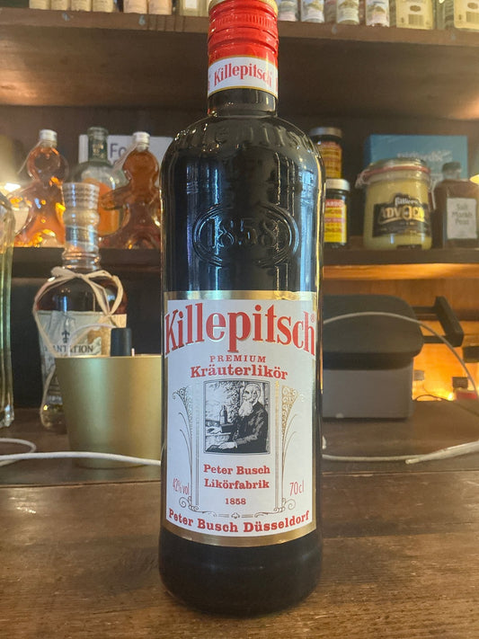 Killepitsch herbal liqueur bottle with red cap, botanical spiced premium small batch specialty spirit on wooden bar counter.