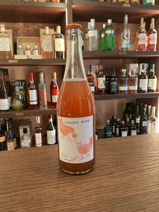 Tall clear bottle of L’étable Fumé non-alcoholic wine with amber liquid, white label featuring elegant orange botanical.
