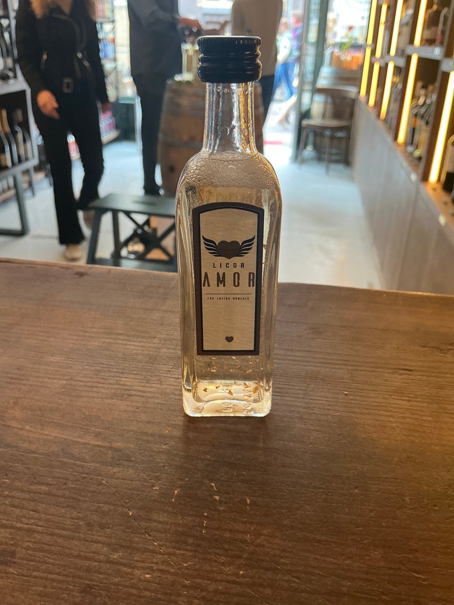 Small clear bottle of Licor Amor miniature cream liqueur with simple beige label and black cap on wooden table in artisan.