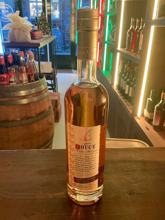 Tall clear glass bottle of Liqueur Douce Eau de Vie de Poire pear liqueur with gold foil neck and detailed white label on.