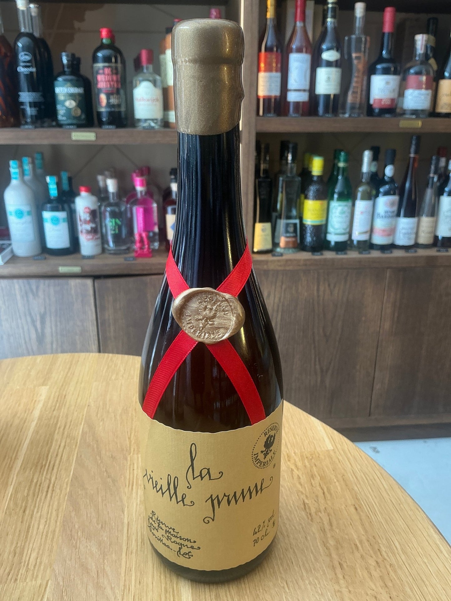 Louis Roque La Vieille Prune Reserve Imperiale plum brandy bottle with wax seal and red ribbon on wooden table, artisan.