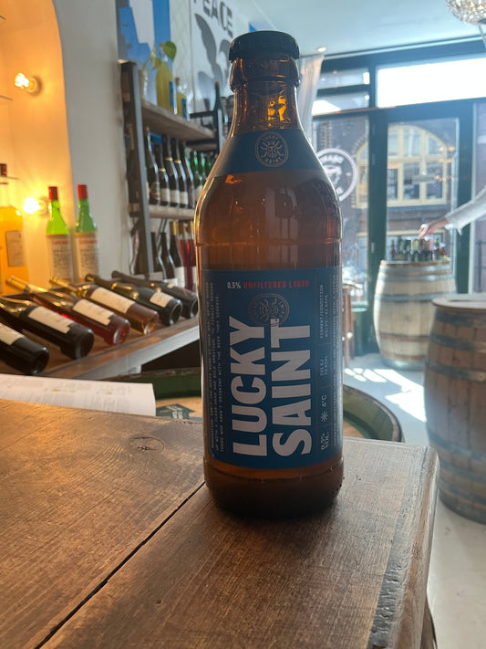 Lucky Saint unfiltered lager bottle with blue label on wooden table in brewery setting, artisan craft beer, premium.