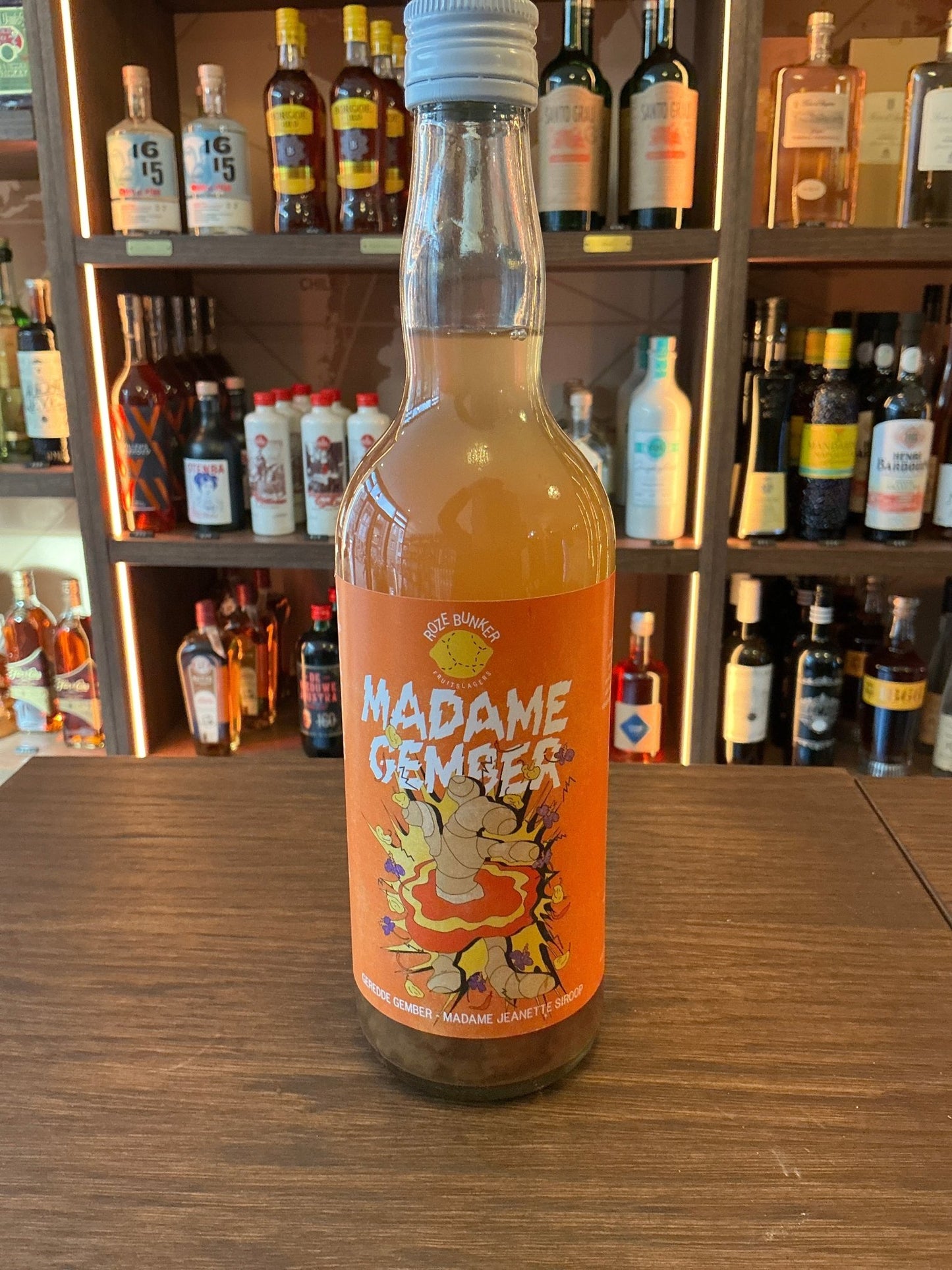 Madame Gember Big cordial bottle with bright orange label featuring artisan botanical and spiced design, displayed on wooden .