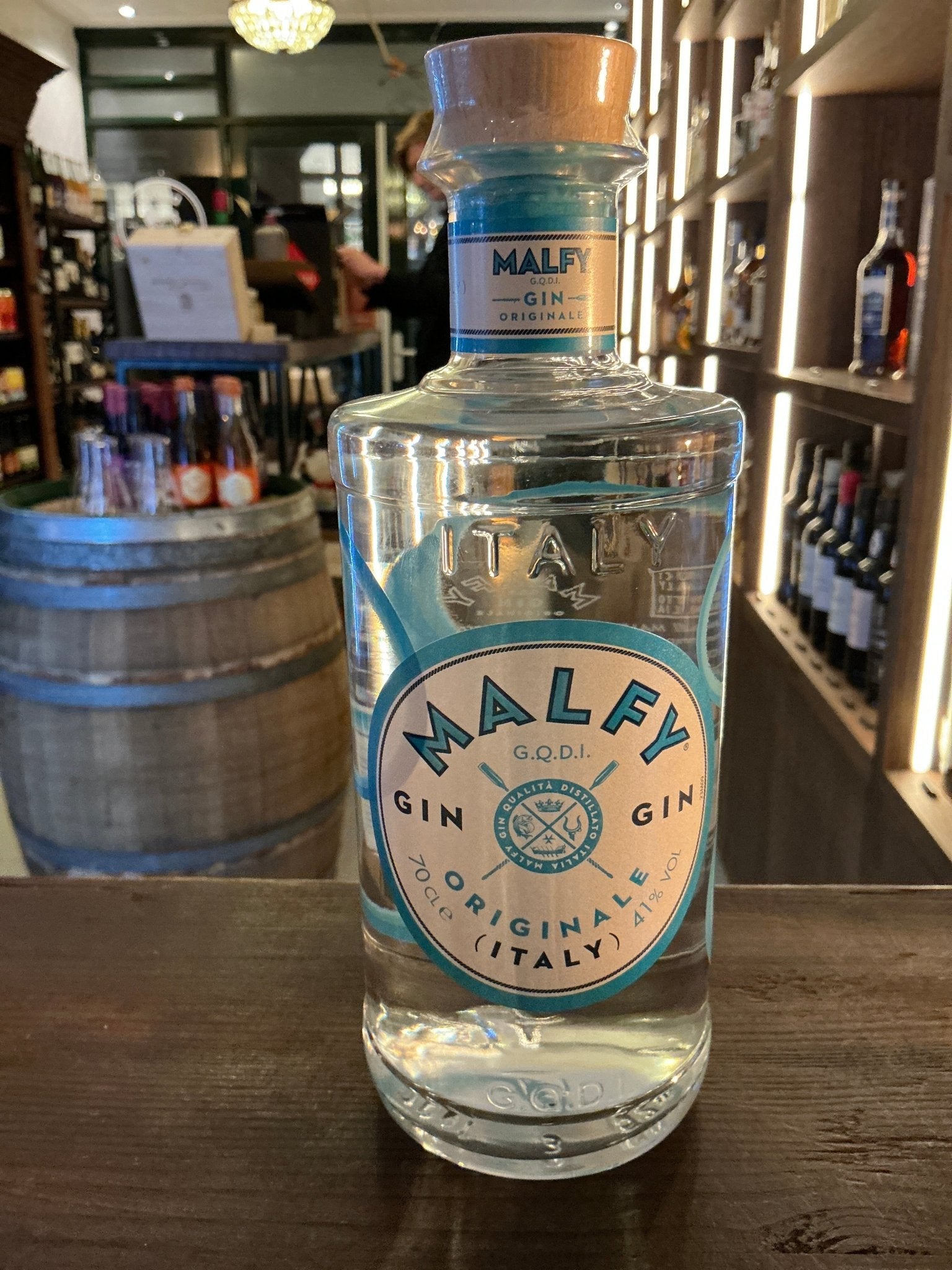 Clear glass bottle of Malfy Gin with blue and white label highlighting its Italian botanical ingredients, displayed on a.