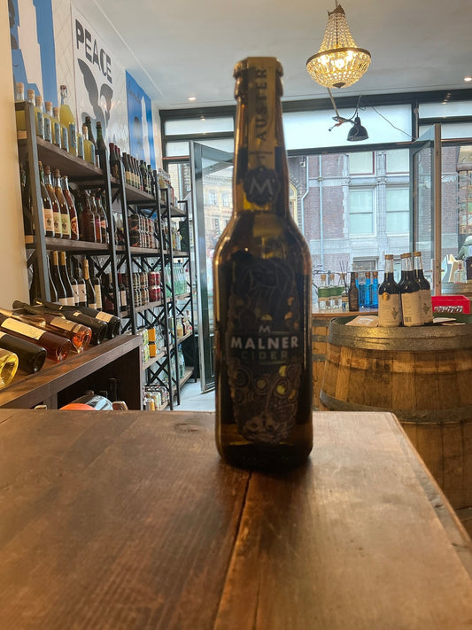 Malner Auster premium small batch cider bottle with dark label and gold lettering on wooden table in artisan spirits shop.