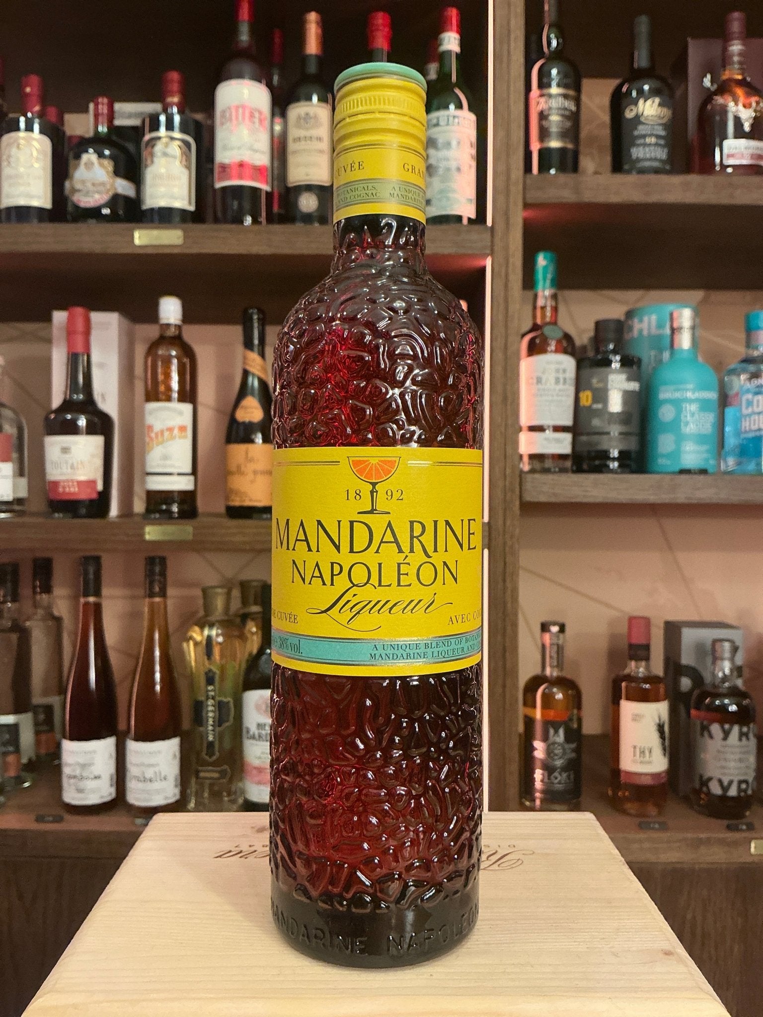 Mandarine Napoleon spiced liqueur bottle with textured design and yellow label featuring premium citrus botanicals on wood.
