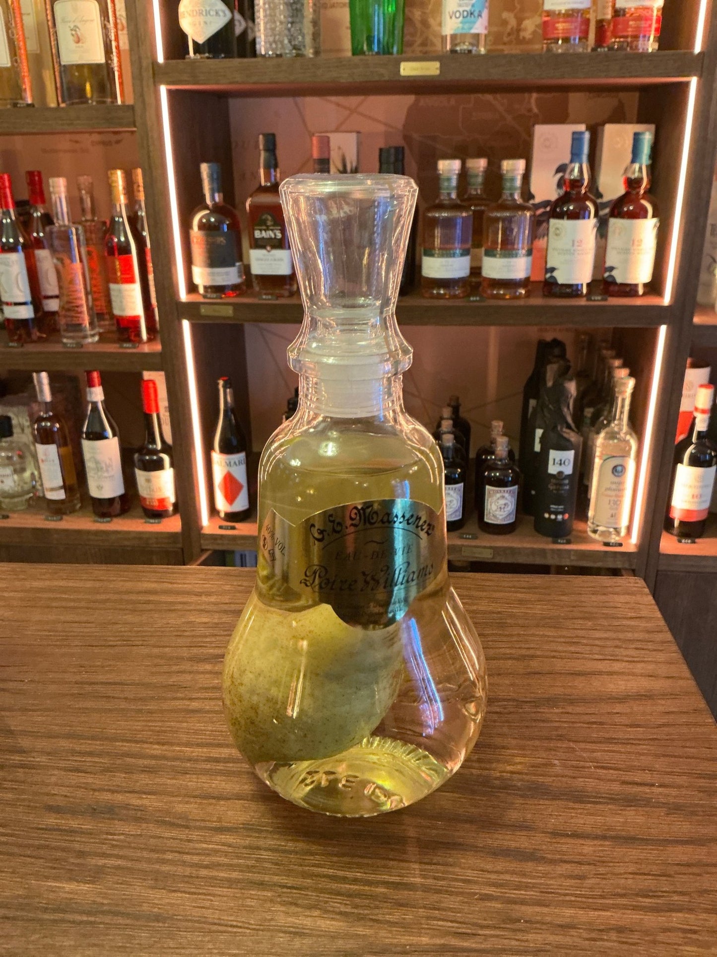 Massenez Poire Prisonniere artisan brandy bottle with whole pear inside, premium distilled fruit liqueur on wooden bar.