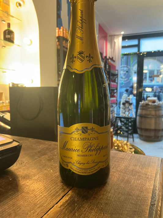Maurice Phillart Carte D’or Brut Champagne 37.5cl bottle with gold foil neck and yellow label on wooden table in warm bar.