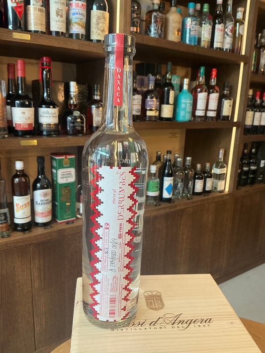 Premium Mezcal Derrumbes No.1 Oaxaca in tall clear bottle with red and white artisanal label, displayed on wooden surface,.