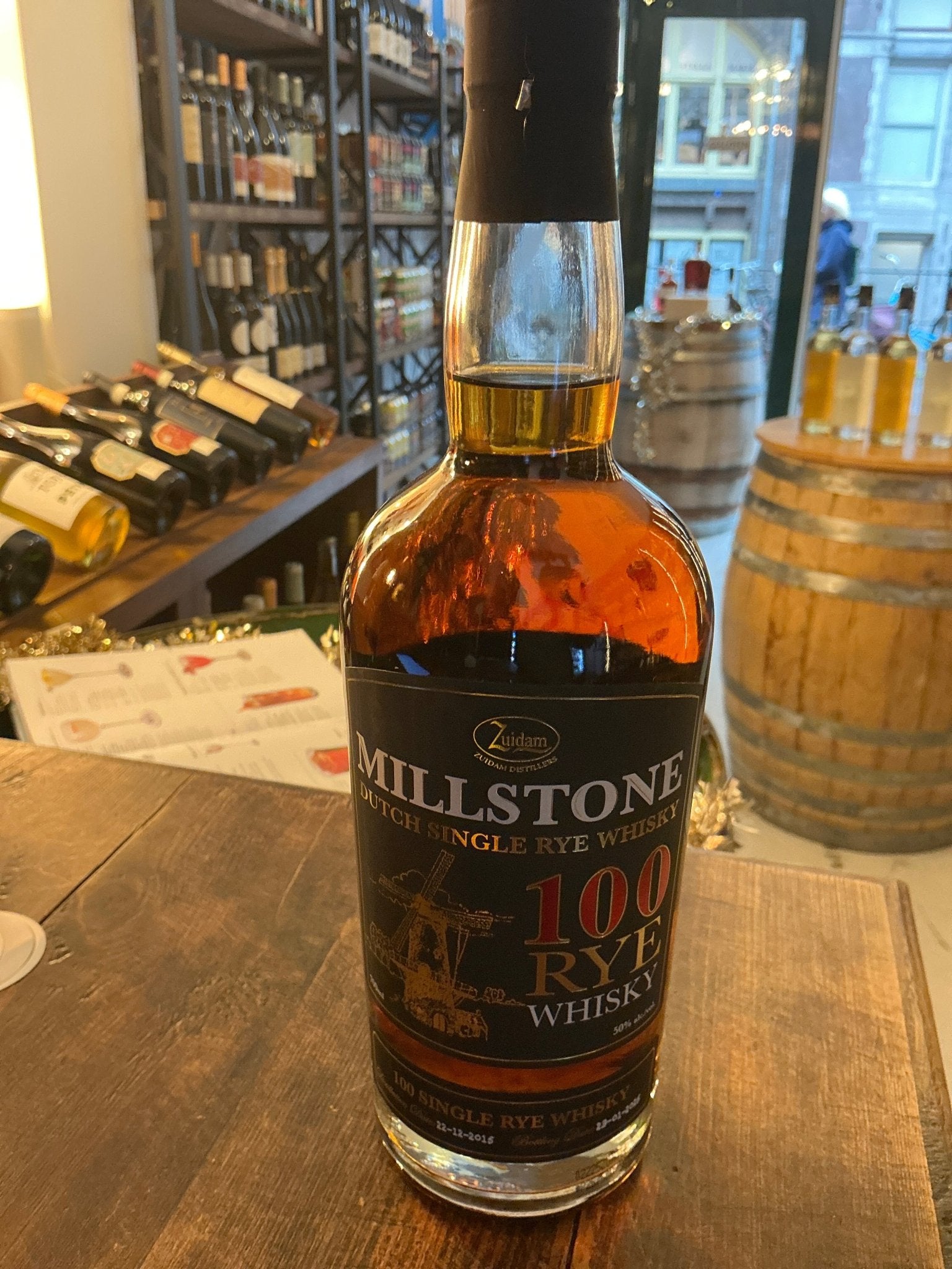 Millstone 100 Rye whisky bottle with amber liquid, premium Dutch small batch spirit, spiced rye flavor, aged and distilled.