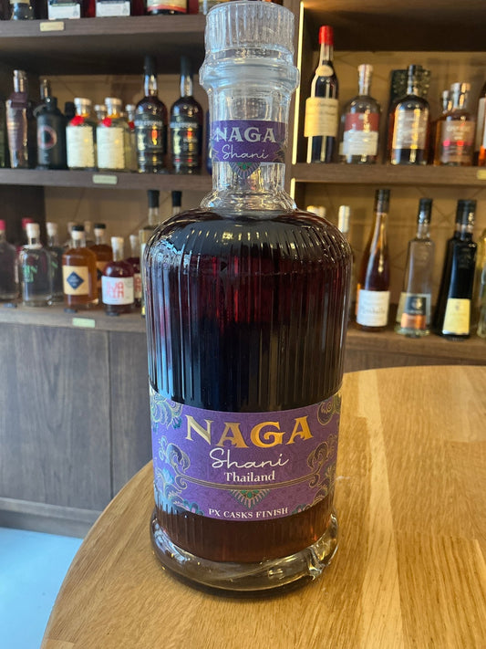Naga Shani Spiced Rum bottle with deep amber liquid, artisan ribbed glass, purple label featuring chili and cacao accents,.