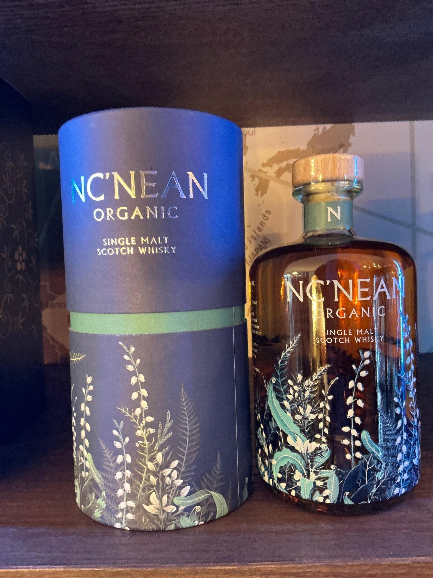 Nc'Nean Organic Single Malt Scotch Whisky bottle with dark brown glass and intricate botanical design, accompanied by.