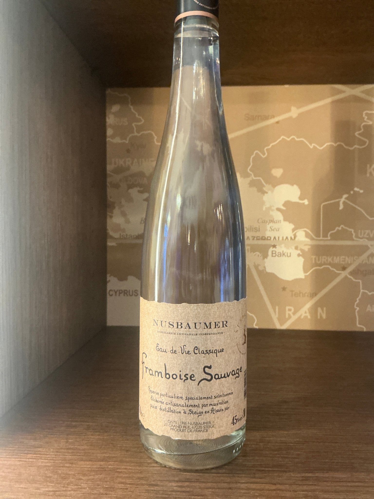 Tall clear glass bottle with a slender neck and silver cap, featuring an artisanal cream-colored label with elegant black.