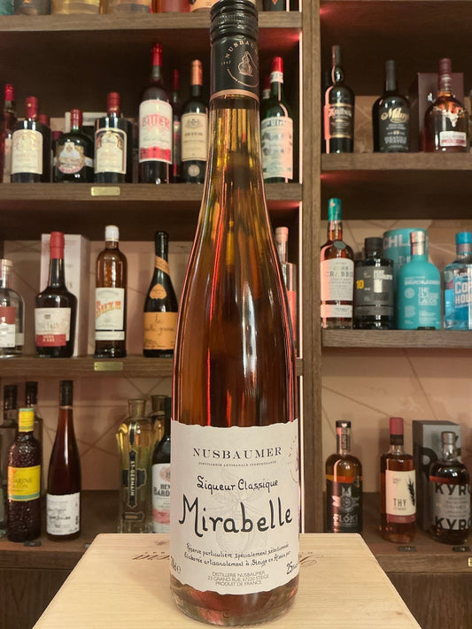 Tall amber glass bottle of Nusbaumer Mirabelle fruit brandy with white label and black cap, displayed on a wooden table with .