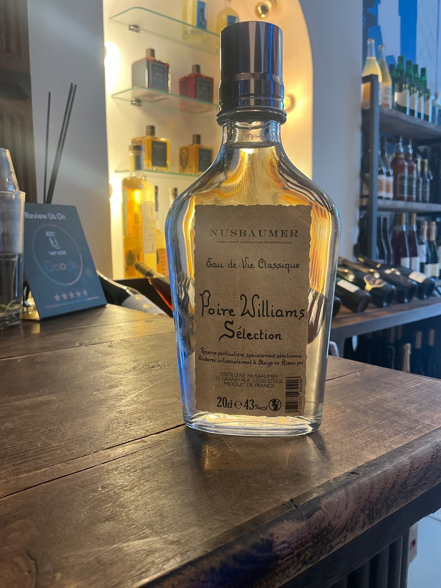 Nusbaumer Poire Williams Sélection clear glass bottle with black cap on wooden bar, premium artisan fruit liqueur, small.