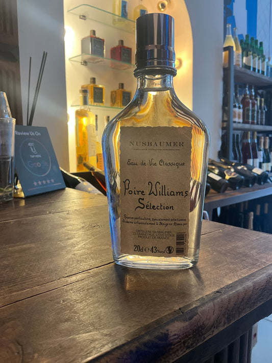 Nusbaumer Poire Williams Sélection clear glass bottle with black cap on wooden bar, premium artisan fruit liqueur, small.