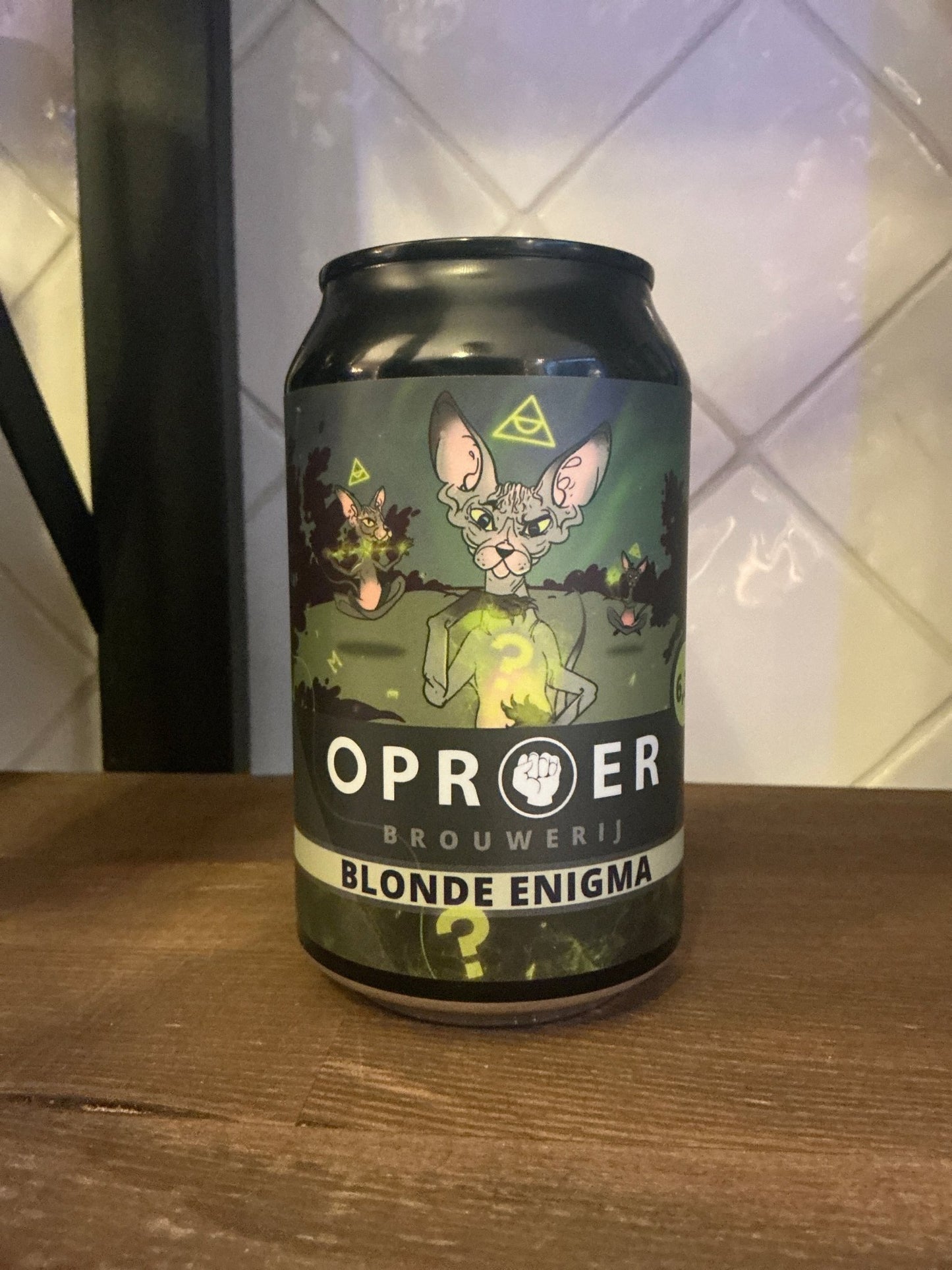 Matte black aluminum can featuring a green and beige artistic label with a mythical creature illustration, labeled Oproer.
