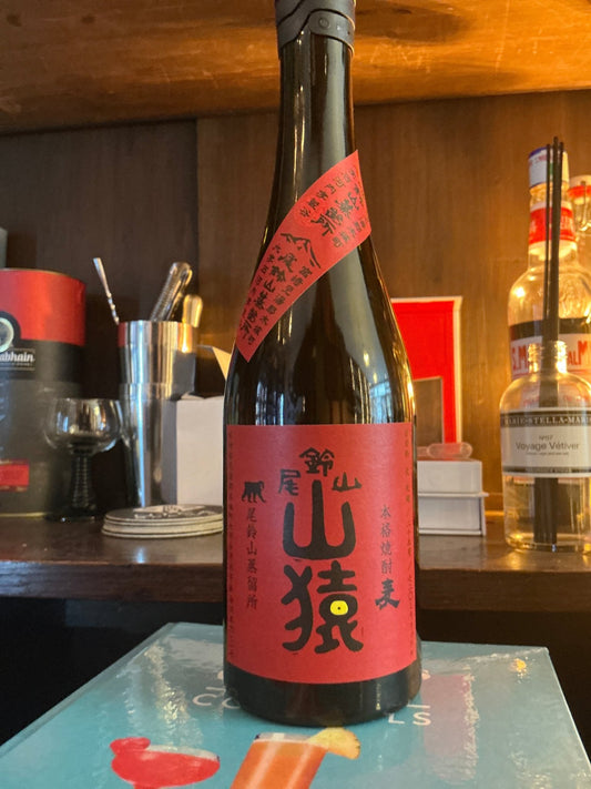 Osuzuyama Yamasaru Barley Shochu premium distilled spiced artisan spirit in tall dark bottle with red label on wooden bar.