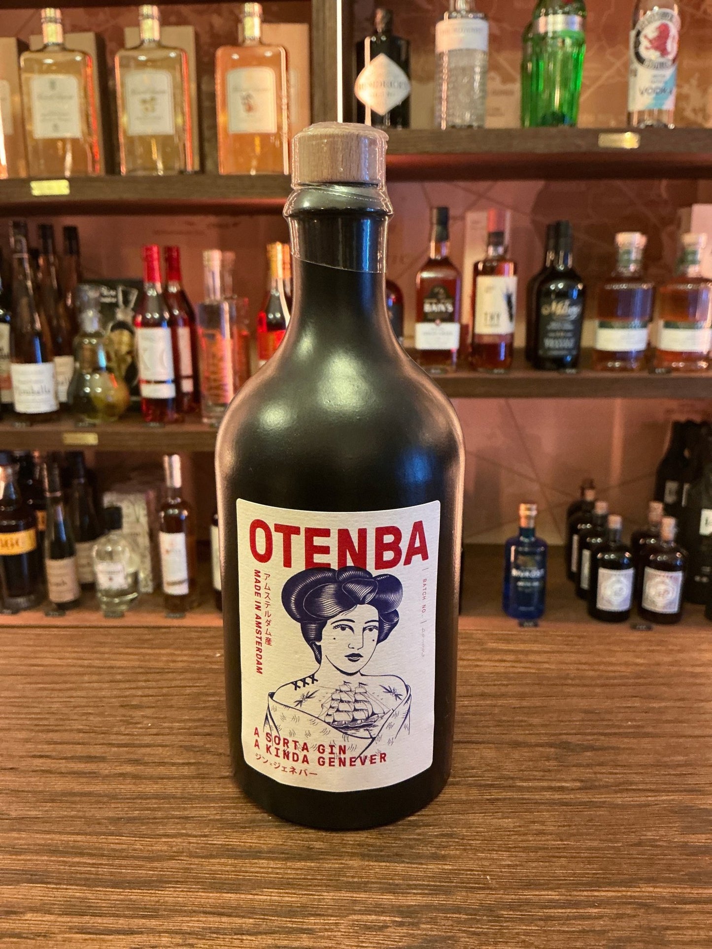 Otenba Gin matte black bottle with red and blue label featuring artisan woman illustration, premium Dutch small batch.
