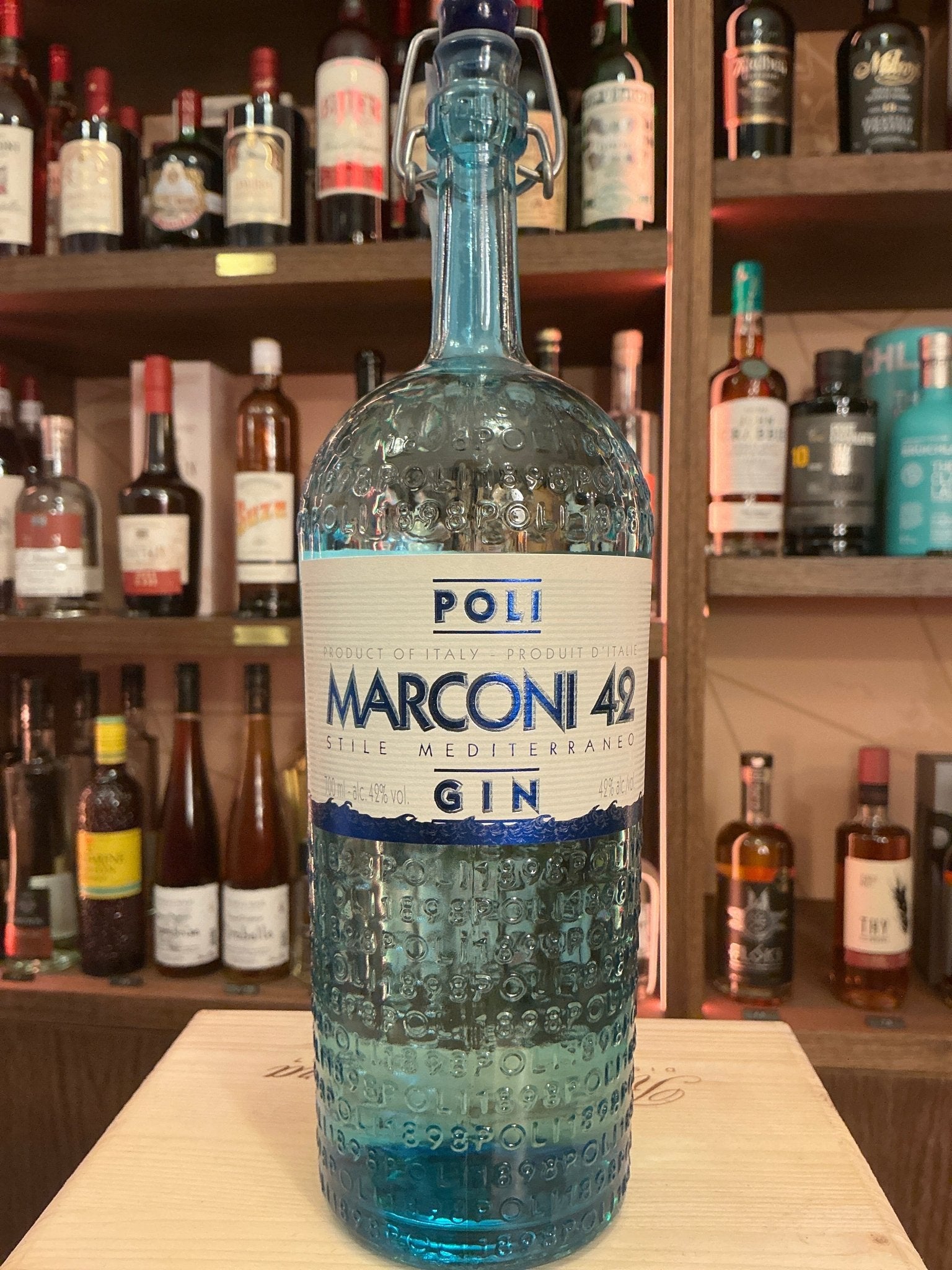Poli Marconi 42 Mediterraneo gin bottle with textured blue glass and white label on wooden bar counter.