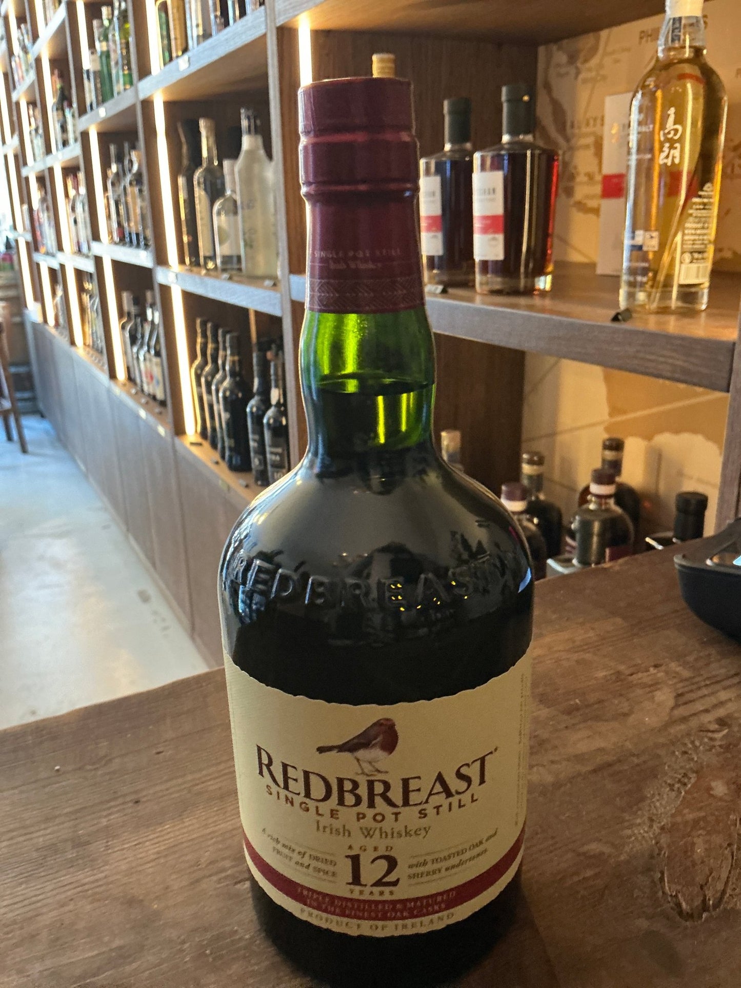 Redbreast 12 Year Aged Single Potstill Irish Whiskey bottle with cream label and maroon cap on wooden counter in liquor.