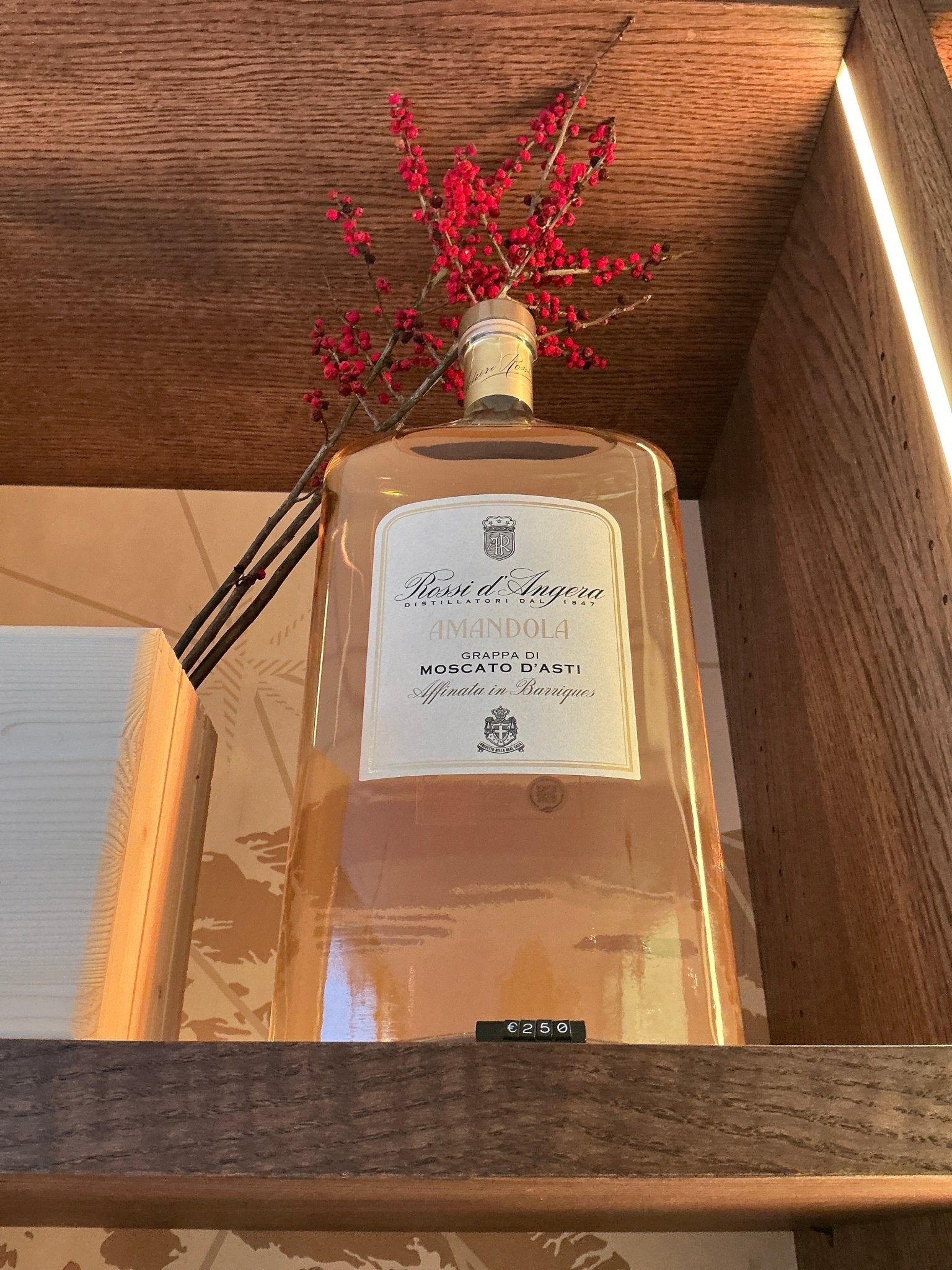 Rossi D’Angera Amandola Moscati D’Asti 3L clear rectangular brandy bottle with cream label and black text on wooden shelf.