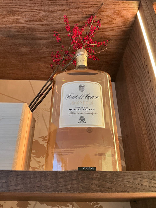 Rossi D’Angera Amandola Moscati D’Asti 3L clear rectangular brandy bottle with cream label and black text on wooden shelf.