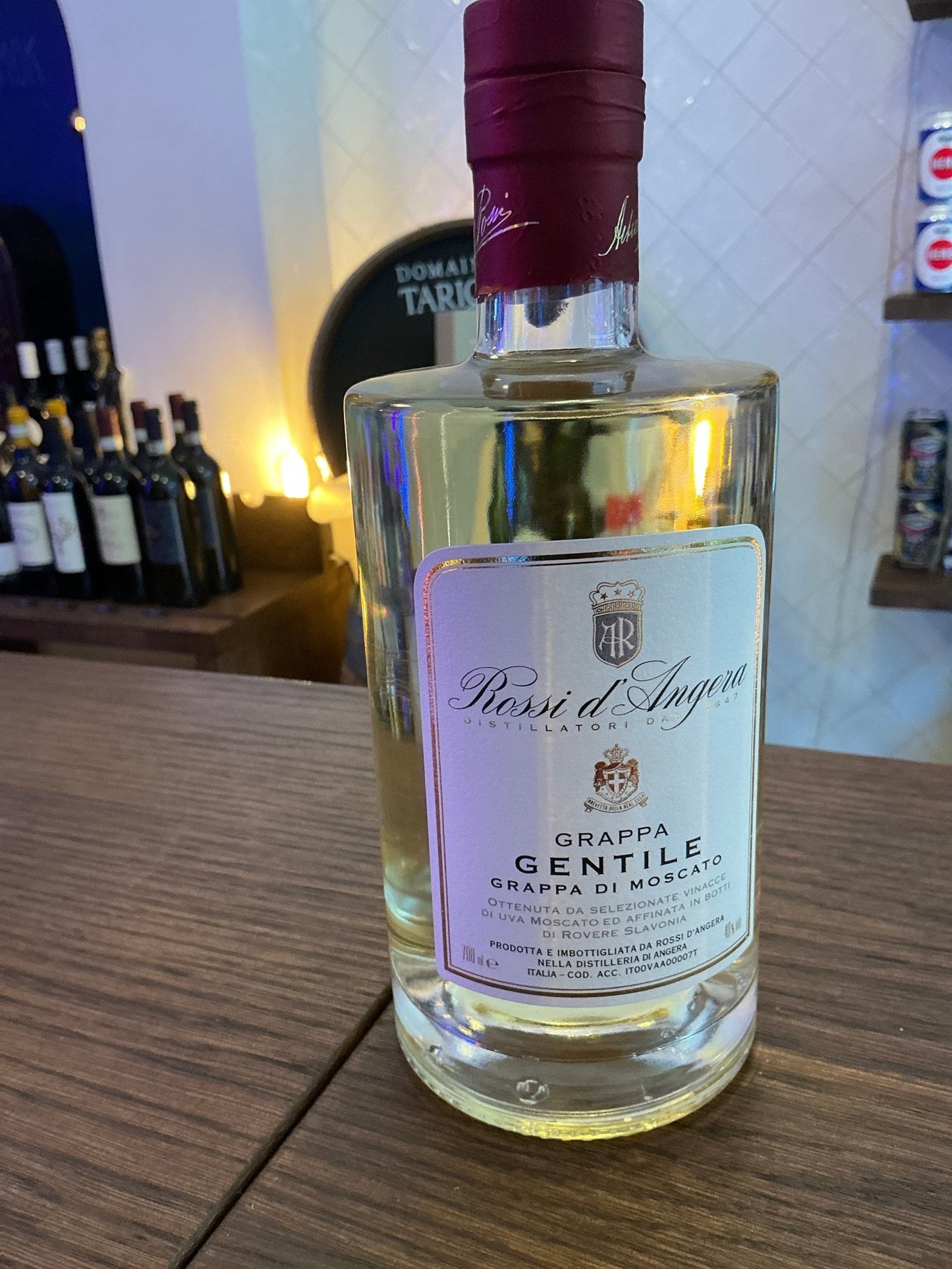 Rossi D’Angera Gentile Grappa premium pomace brandy in clear glass bottle with maroon cap and white label on wooden surface.
