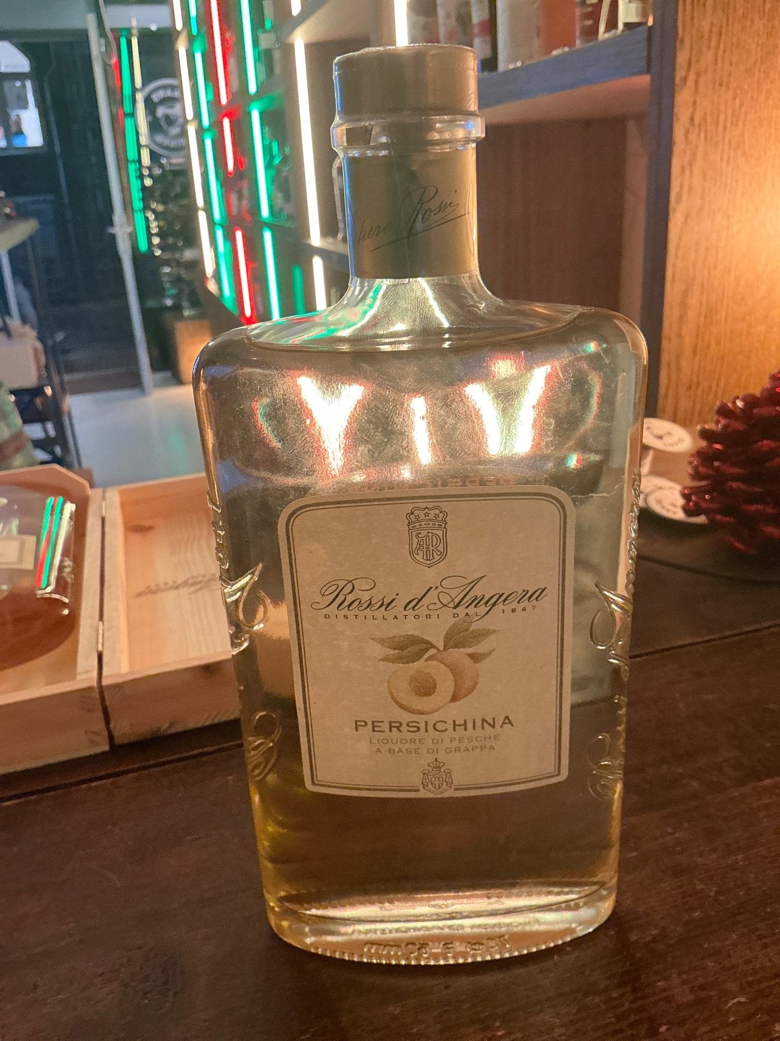 Rossi D’Angera Persichina grappa bottle with clear glass, square shape, beige label, and gold foil cap, premium artisan.