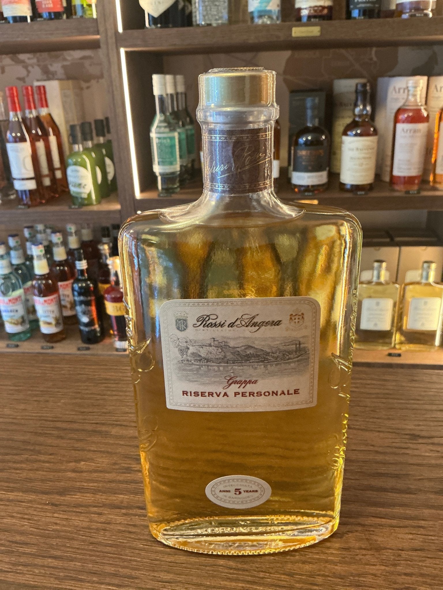Rossi D’Angera Riserva Personale premium aged grappa bottle with golden amber liquid and elegant label on wooden bar shelf.