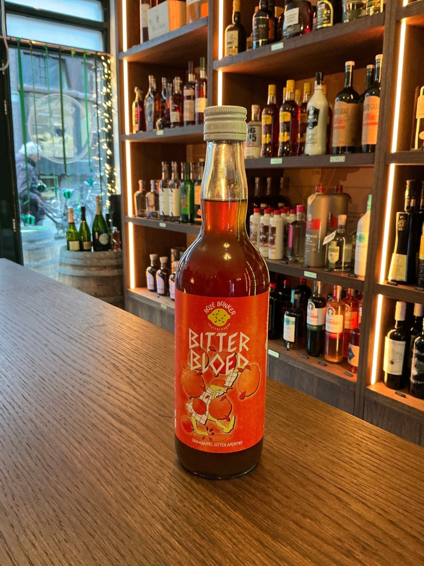 Roze Bunker Bitter Bloed spiced cordial bottle with vibrant orange label on wood counter, artisan Dutch specialty spirit.