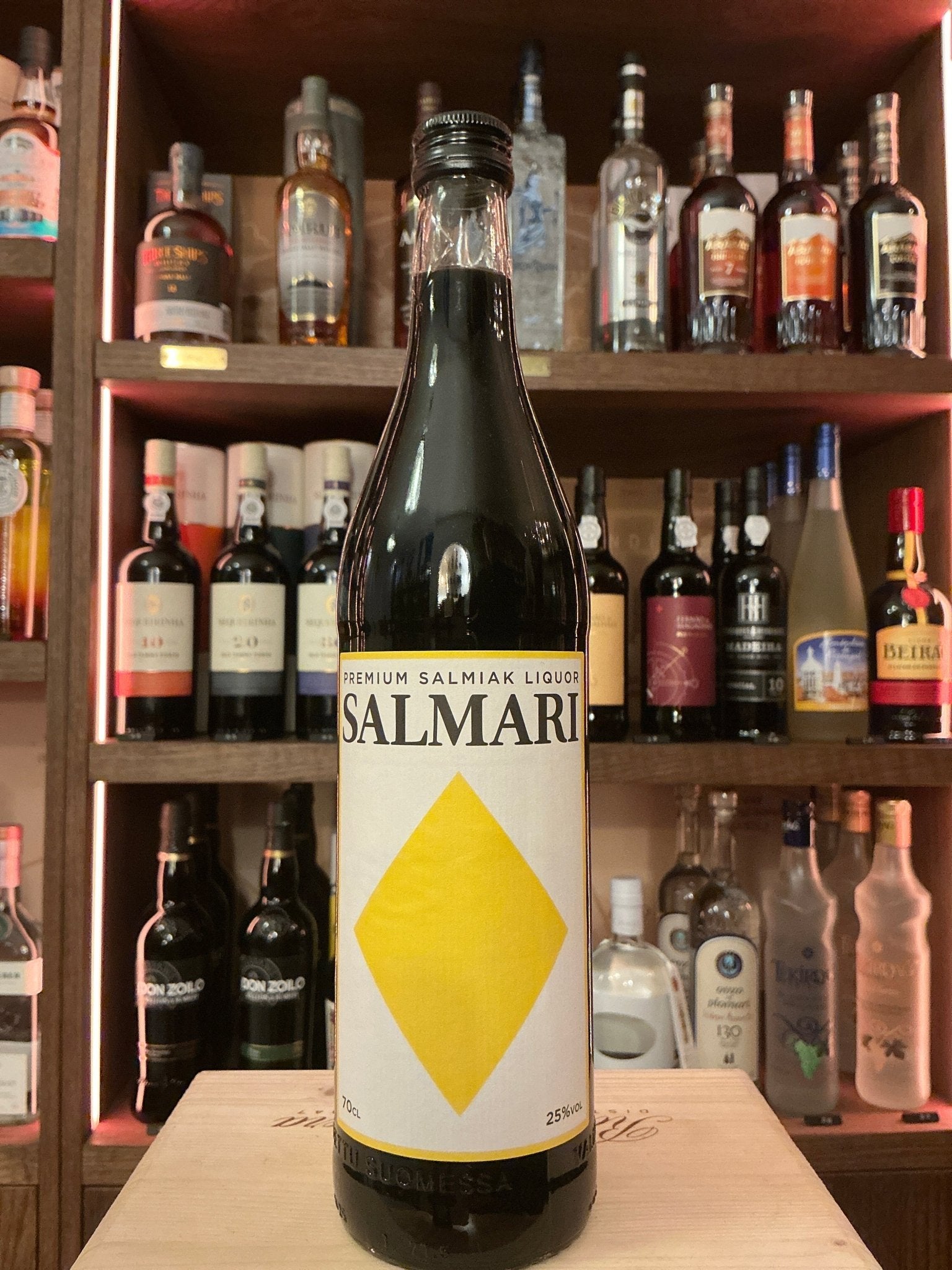 Tall brown glass bottle of Salmari Liquorice Liqueur with white label featuring bold yellow diamond, set against shelves of.