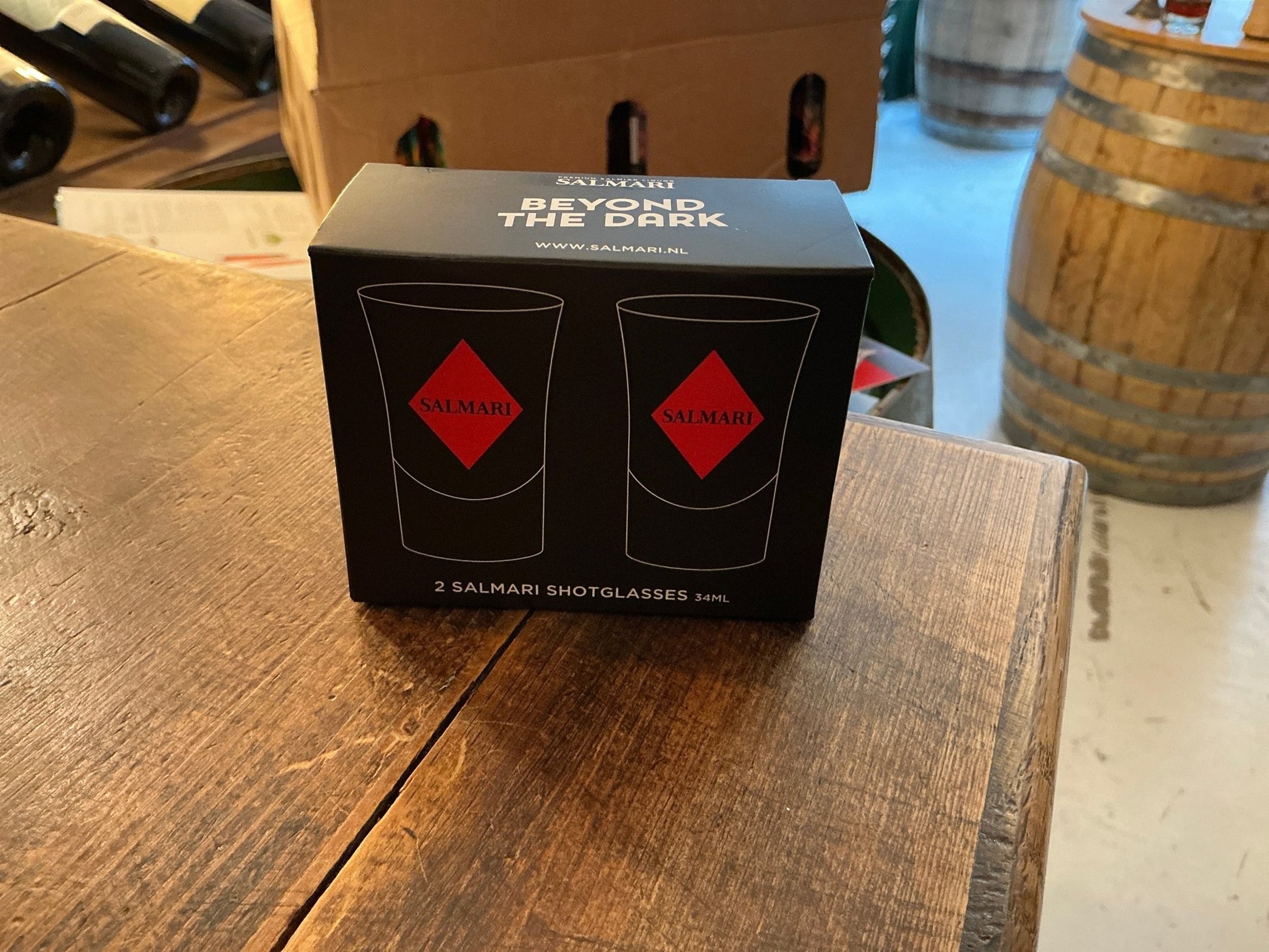 Black and red Salmari branded box with two illustrated shot glasses placed on a rustic wooden table surrounded by wooden.