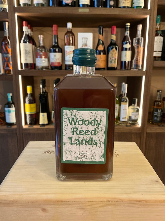Square brown glass bottle of Salt Marsh Peat non-alcoholic spirit with green label reading "Woody Reed Lands" on wooden.