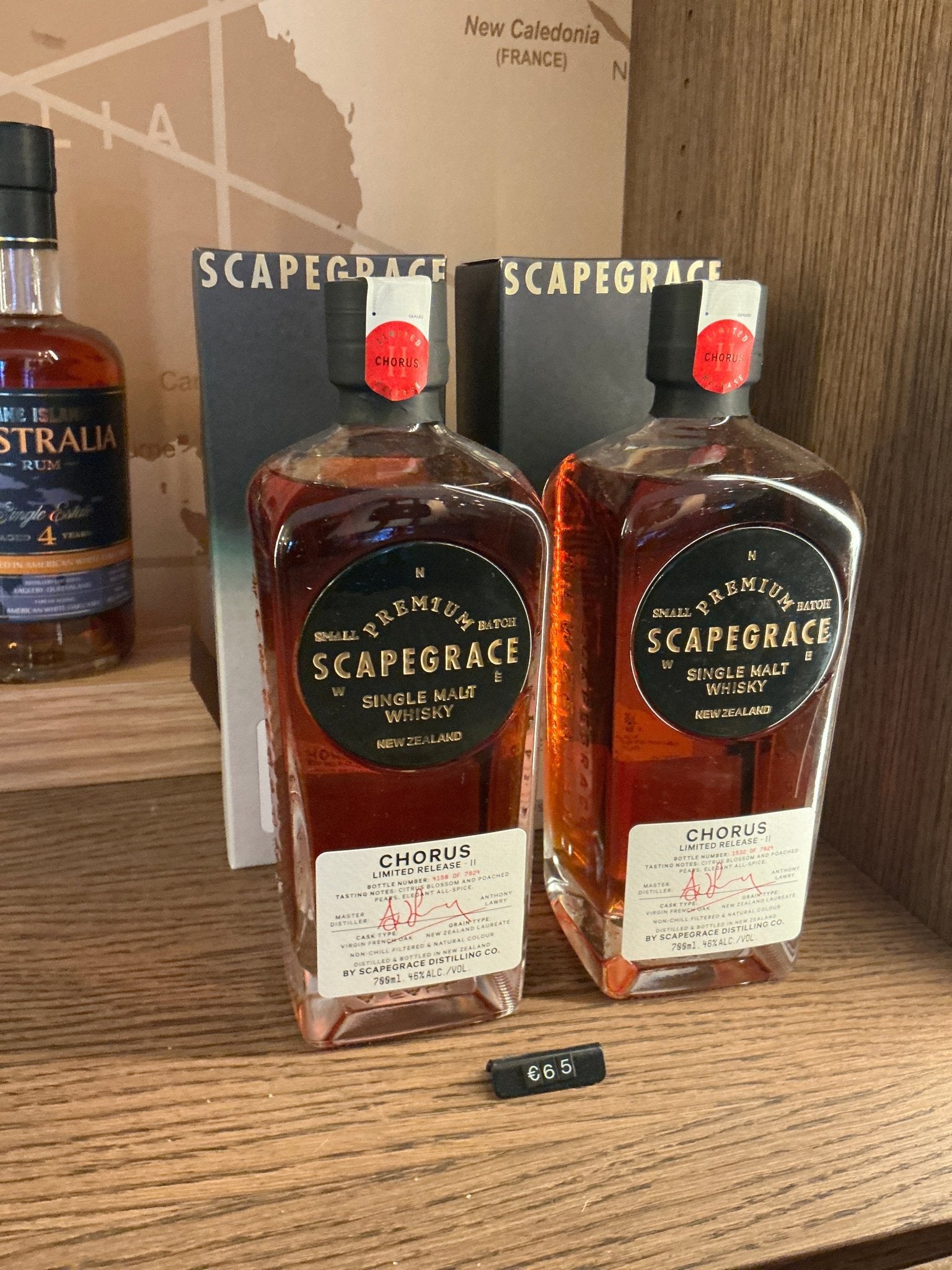 Two rectangular bottles of Scapegrace Chorus Single Malt whisky, amber liquid inside, black and gold labels with red caps,.