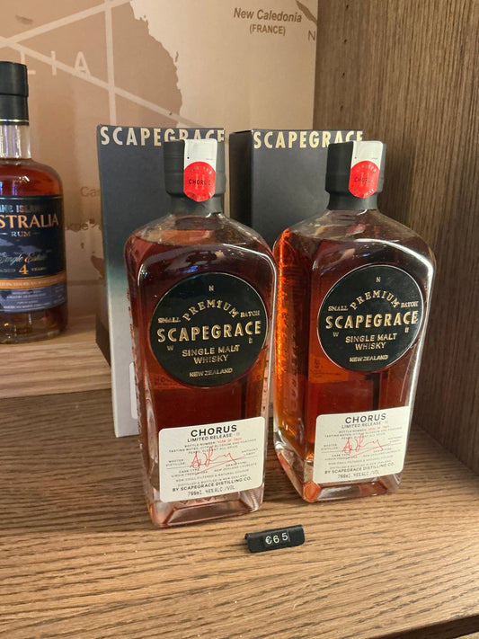 Two rectangular bottles of Scapegrace Chorus Single Malt whisky, amber liquid inside, black and gold labels with red caps,.