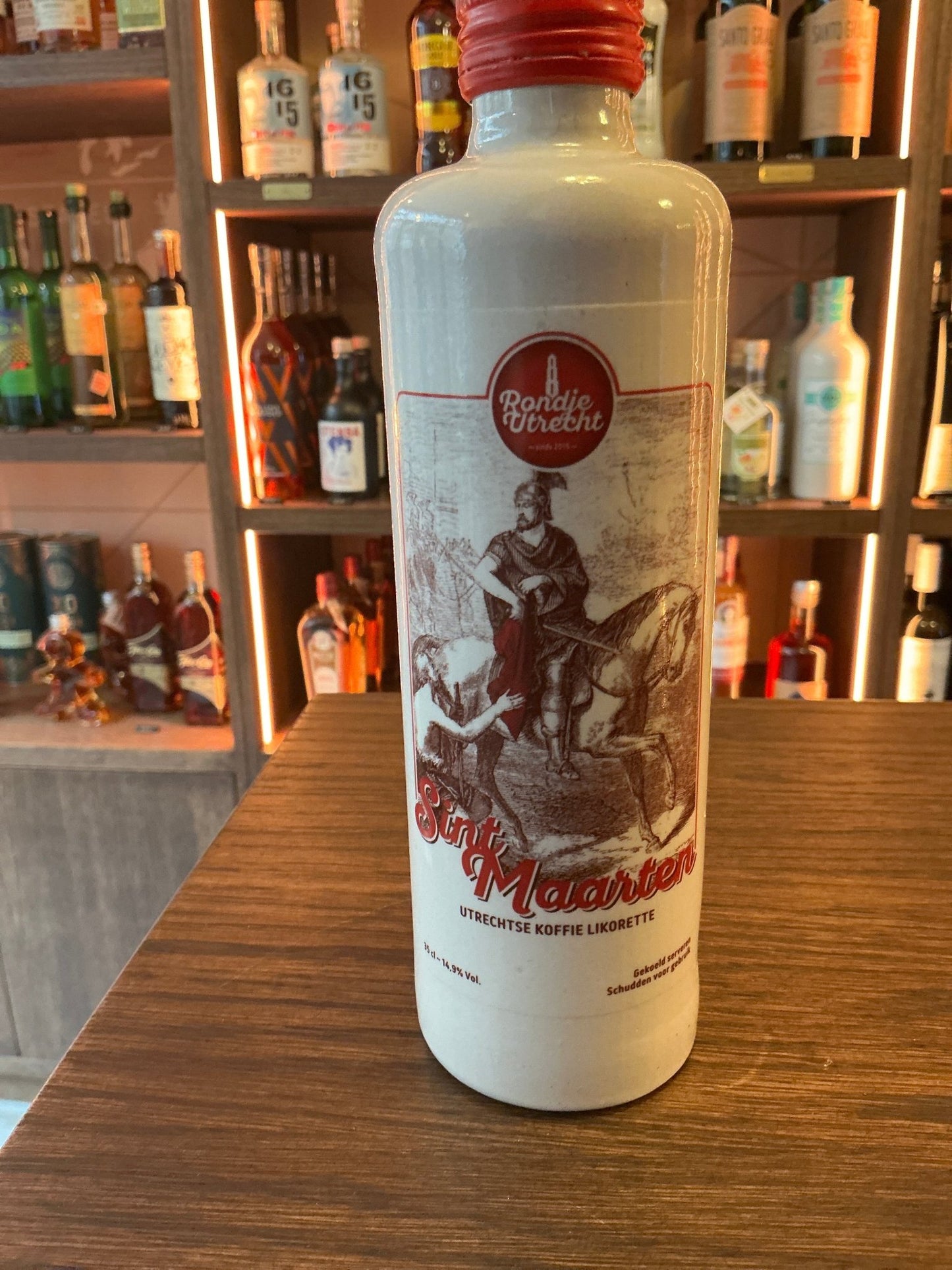 White ceramic bottle of Sint Maarten artisan chocolate liqueur with red cap and vintage-style label on wooden table in bar.