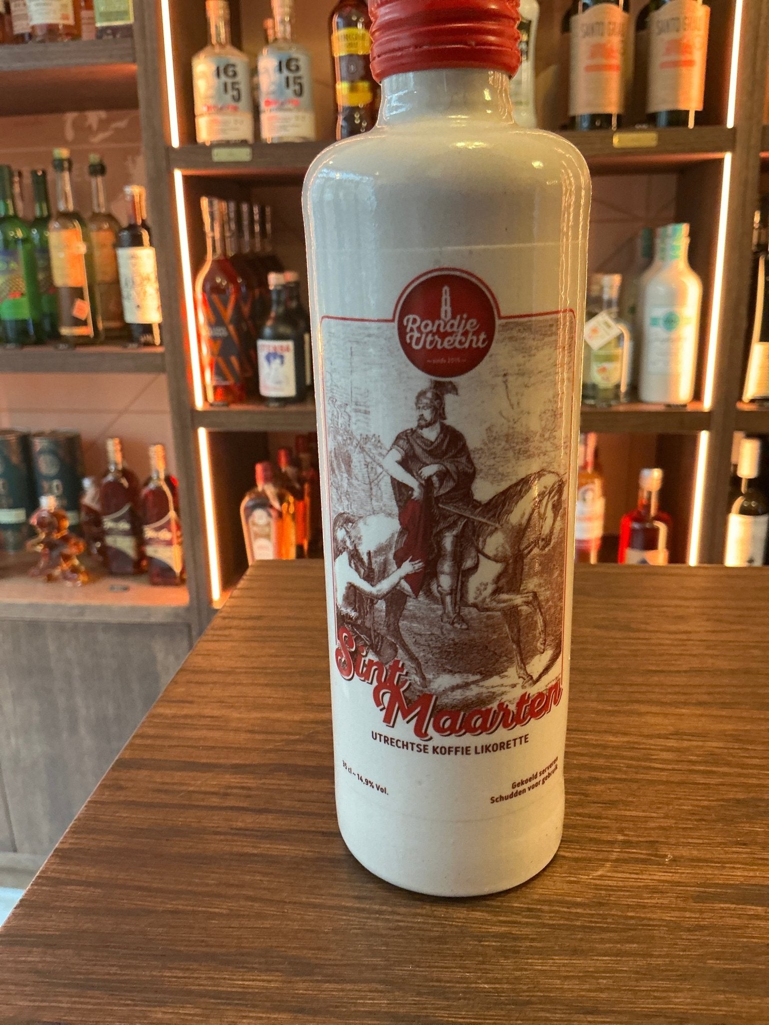 White ceramic bottle of Sint Maarten artisan chocolate liqueur with red cap and vintage-style label on wooden table in bar.