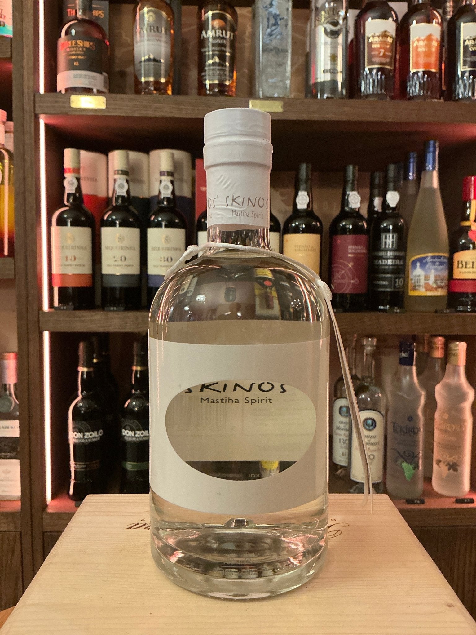 Clear bottle of Skinos Mastiha liqueur with white label and cap, botanical premium spirit on wooden surface, artisan small.