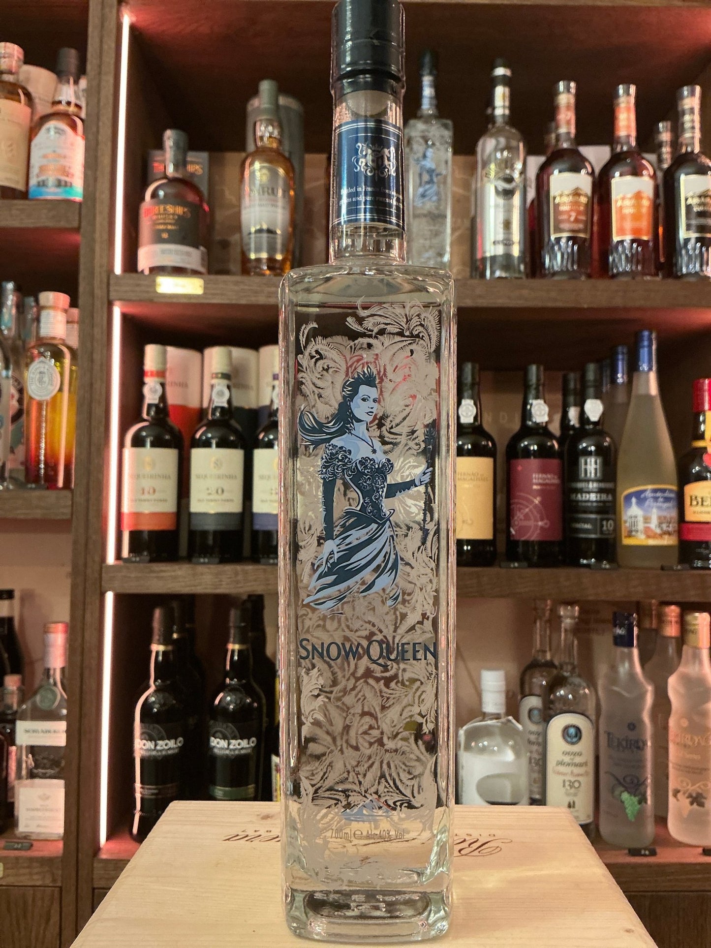 Tall clear glass bottle of Snow Queen vodka with intricate blue and silver icy design and black cap, displayed on wooden bar .