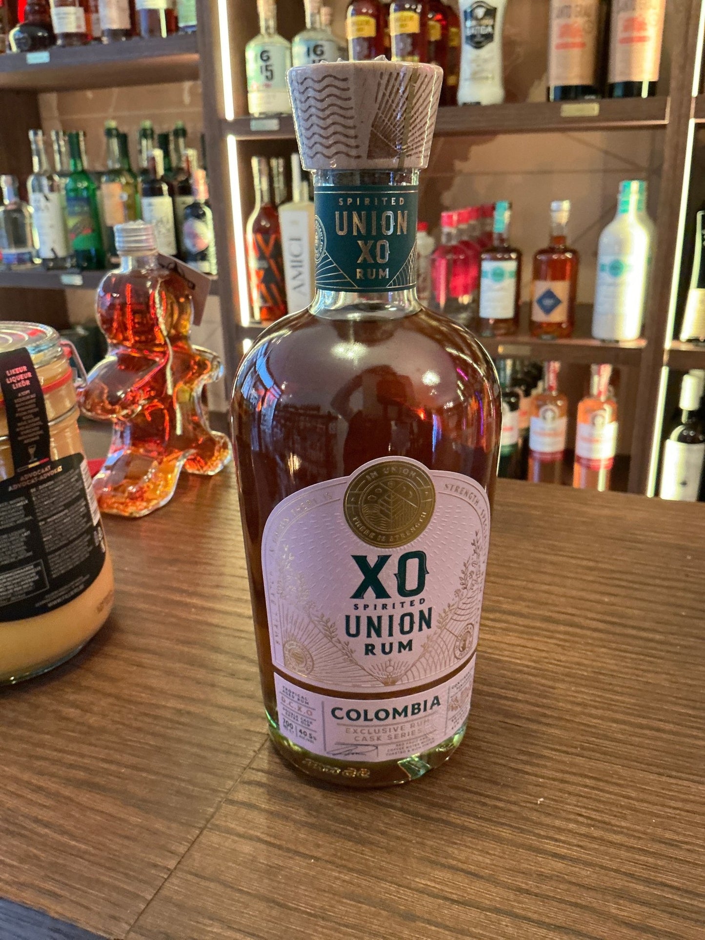 Spirited Union XO Colombia aged rum bottle with embossed seal and textured cap on wooden bar surface, premium artisan spirit.