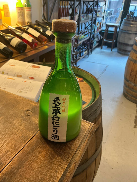Green glass bottle of Tenjo Mugen Nigori Junmai Ginjo sake with cork stopper, artisan Japanese premium spirit on wooden.